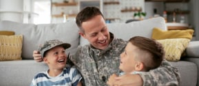 Soldier and his little son hugging at home. Smiling soldier reunited with his son after coming back from war. Military soldier father with son kid smiling during home return - Family love US army