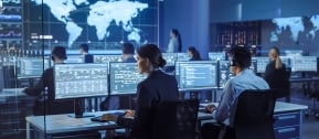 Serious female agent of intelligence service sitting in front of computer monitors in office and processing personal data of criminals