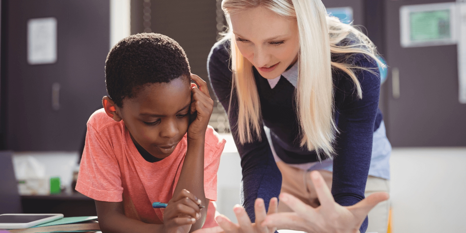 Stock image: Bored schoolboy looking away while sitting at desk with girl in background at classroom | By: Tyler Olson