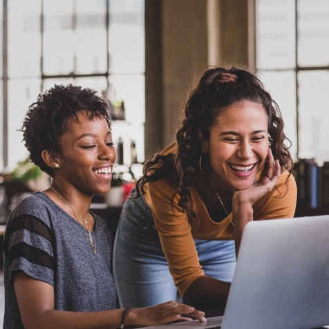 Two women smiling while watching something in a laptop